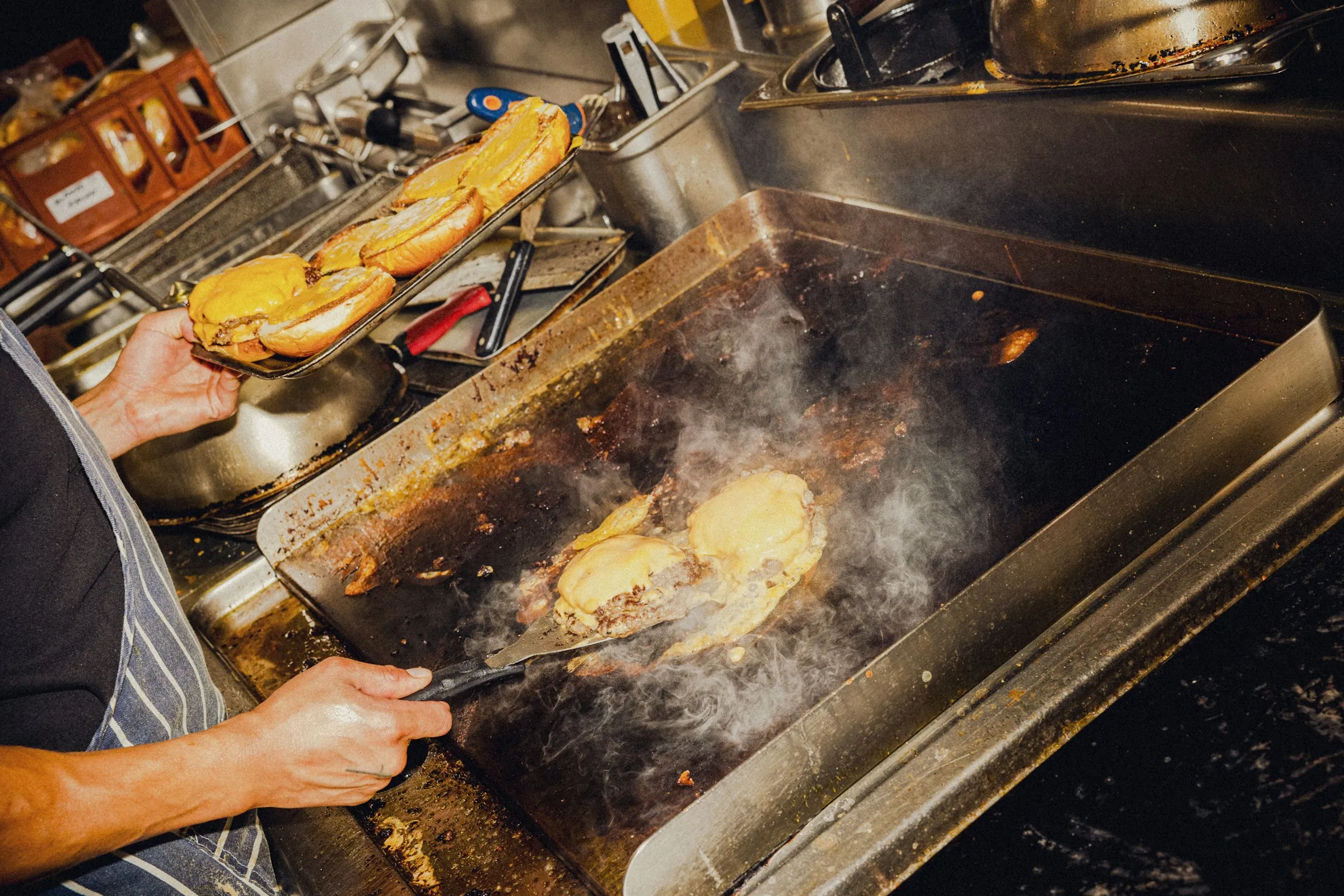 A cook pressing smash burgers on a flat-top grill in a restaurant kitchen