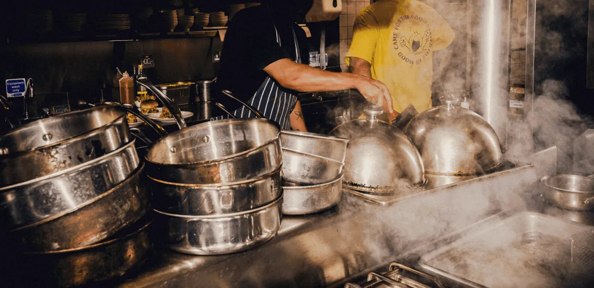 Steam rising off stacked steel pots in a busy restaurant kitchen
