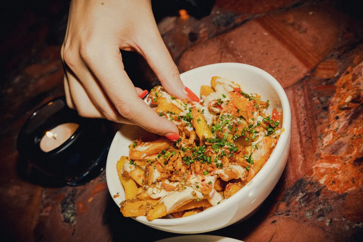 A hand reaching into a bowl of loaded fries