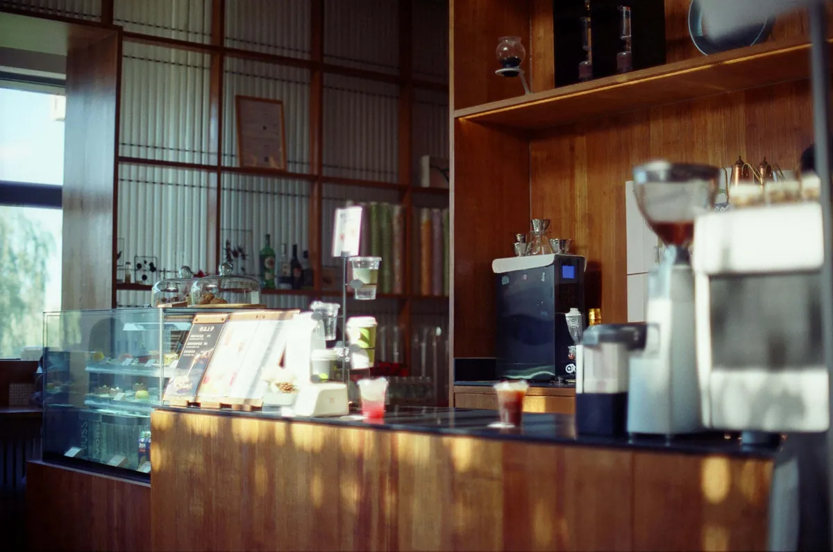 A sunlit cafe counter with a pastry case and espresso grinders