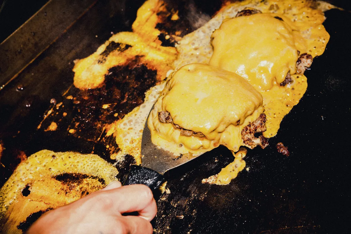 Melted cheese over smash burgers on a flat-top grill